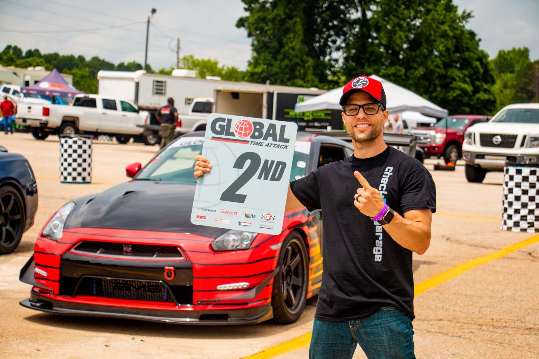 Jason holding a Global Time Attack 2nd place sign beside his red and black Nissan GT-R
