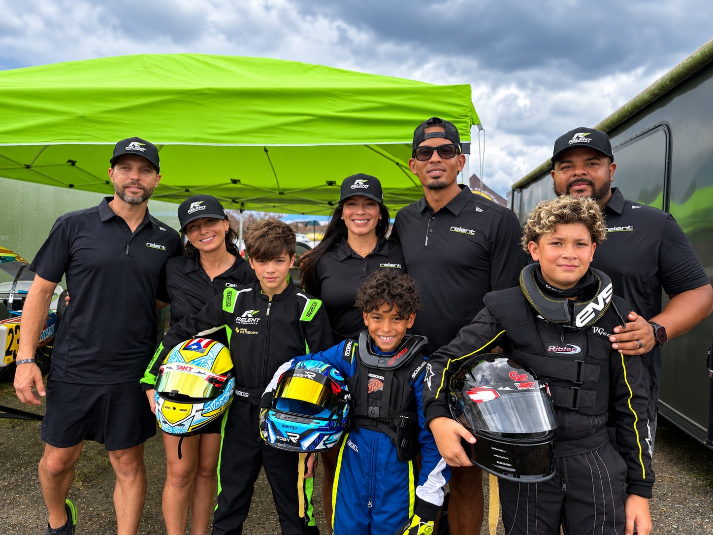 Relent Motorsports crew, families and young drivers with their helmets under the green team tent